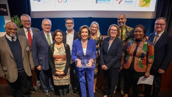 Nancy Pelosi stands onstage holding an award, surrounded by UCSF leadership and facutly.