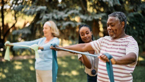 A middle-aged African-American man and Caucasian woman receive coaching from a young Black coach on how to properly use their exercise bands.