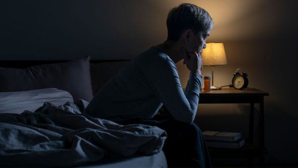 A woman who is unable to sleep sits at the edge of her bed in the middle of the night.