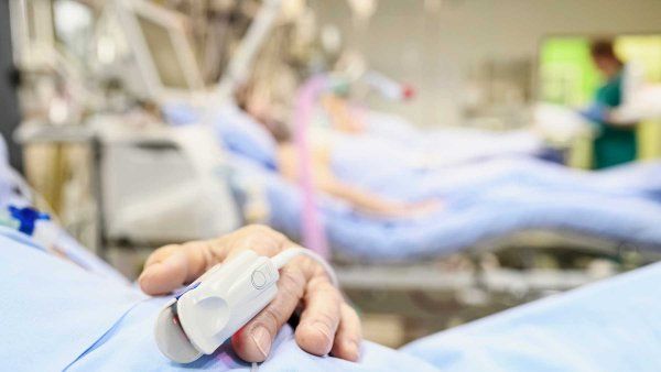 A patient wears a pulse oximeter as they lie in a hospital bed at an intenstive care unit.