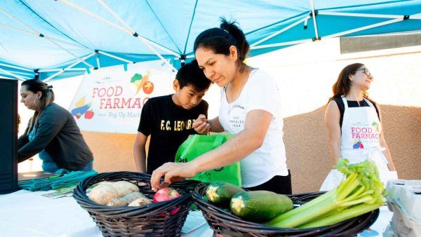 A Latino mother and her son collect fresh vegetables at a food clinic.