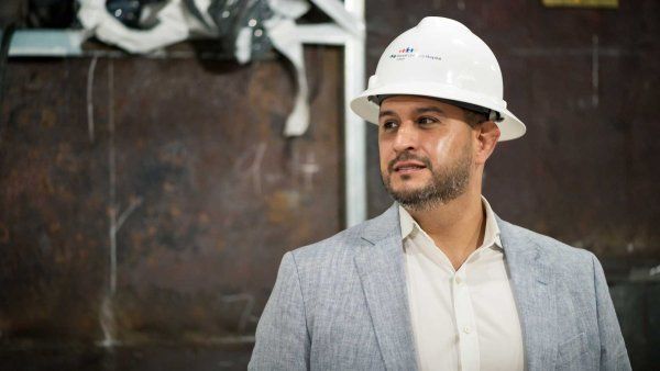 Construction project manager Michael Valero stands inside a construction zone and wears a white construction hat with the UCSF Benioff Children's Hospital Oakland logo on it.