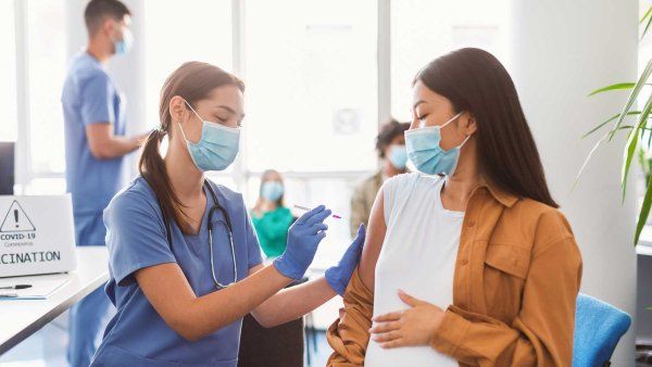 A pregnant woman wearing a surgical mask recieves a vaccine from a nurse.