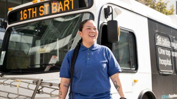 Shuttle driver stands in front of bus smiling