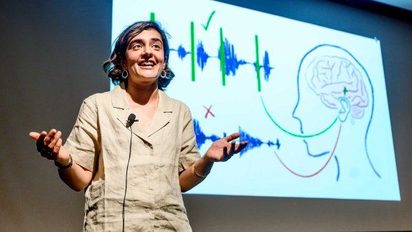 2024 Grad Slam winner Ilina Bhaya-Grossman presents her research onstage. In the background is a presentation slide showing an illusration of measurements of brainwaves.