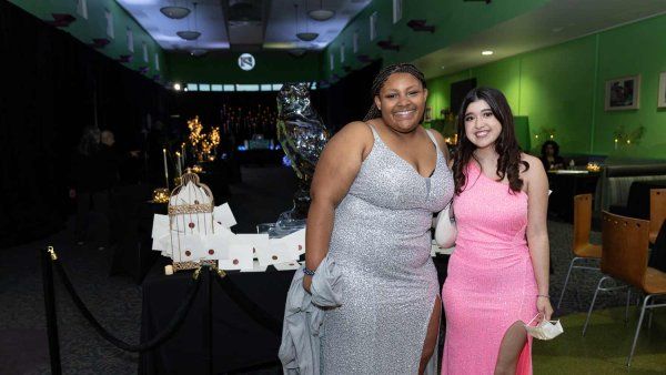 Two teenage girls pose together at the U C S F Benioff Children's Hospital prom event. One has a silver evening gown, and the other a pink one.