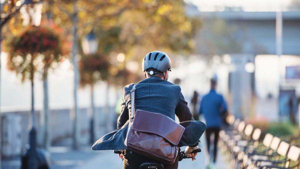 A business man rides a bike across a park-lined street on his way to work.