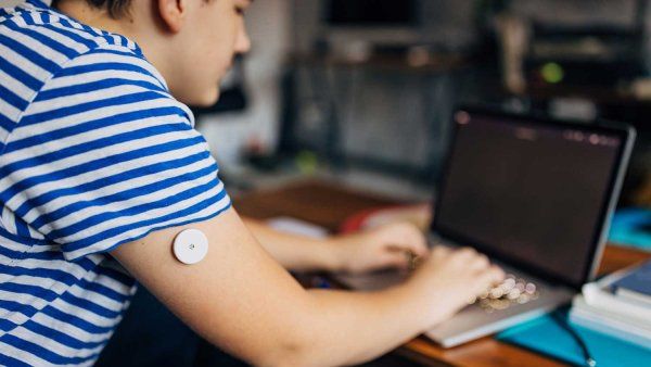 A boy wearing a diabetic patch on his arm uses a laptop.