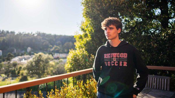 A young teenage boy named Marcos Ornellas stands outside on a deck and looks off into a hilly view.