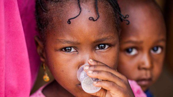 A small African girl drinks medicine from a small cup.