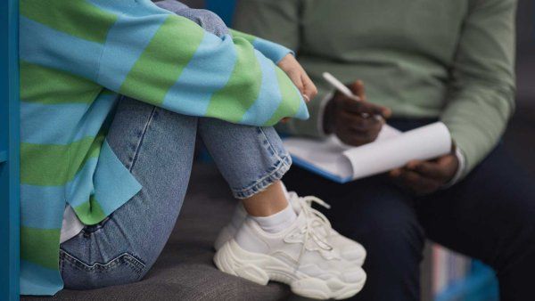 A therapist takes notes while they speak with a young patient.