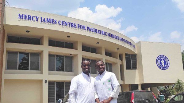 Doctros Alliance Niyukuri and Bienvenu Mbida stand together outside a pediatric srugery center in Malawi.