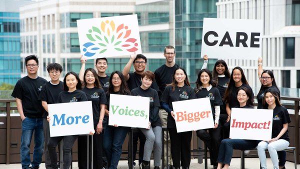 A group photo of the CARE team, who all wear CARE T-shirts and hold up signs that read "CARE" and "more voices, more impact."