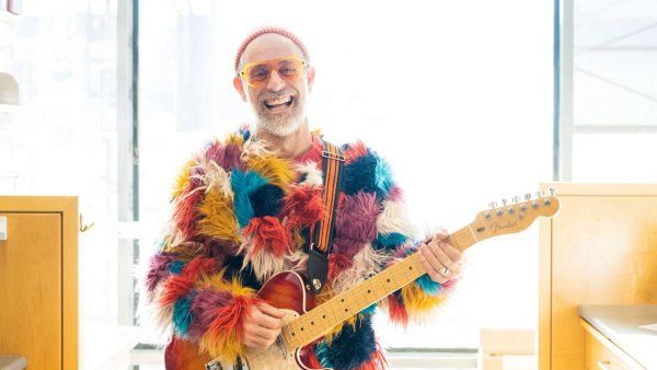 Man plays electric guitar in laboratory wearing colorful fluffy coat.