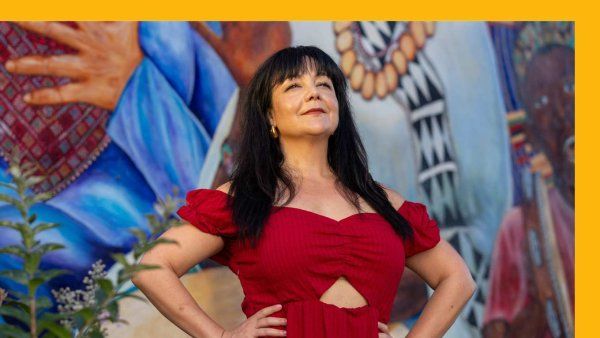 Sophia regally looks up in a red dress with colorful mural behind her.