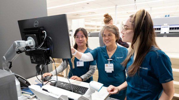 Three pharmacy staff members smile together as they look at information on a computer screen at the new pharmacy in Mission Bay.