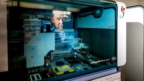 Researcher Charles Chiu is pictured in the reflection of a robotic machine used to extract DNA from a sample.