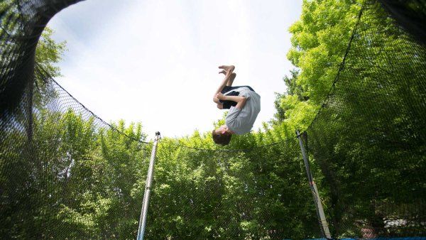 A young boy hangs upside down in middair as he jumps on a trampoline.